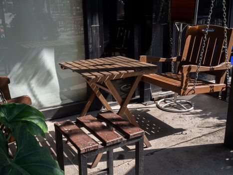 Wooden table, wooden chair and wooden swing in the backyard. Shady place for relaxation.