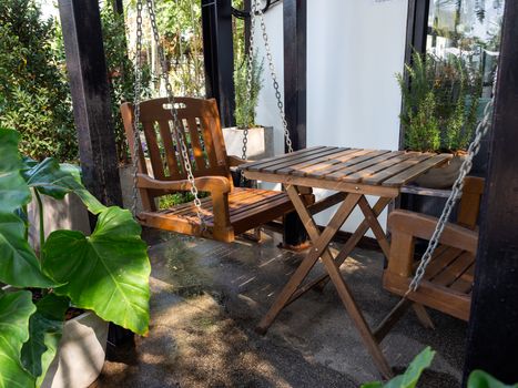 Wooden table, wooden chair and wooden swing in the backyard. Shady place for relaxation.