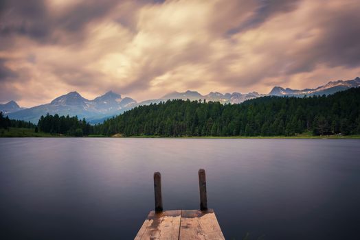 Wooden pier at the Lake of Staz near St. Moritz in Switzerland with Swiss Alps in the background. This lake is also known as Stazersee and Lej da Staz. Long exposure.