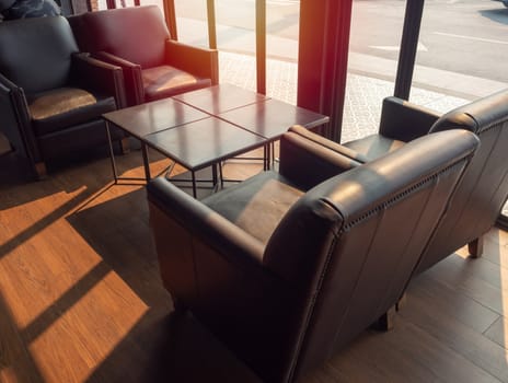 Brown leather sofa with wooden table on wooden floor near glass window in cafe on sunshine day.