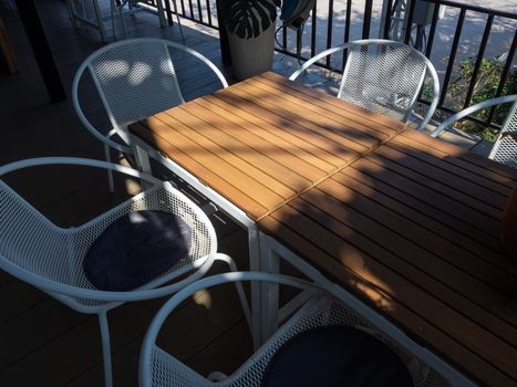 Wooden table and white retro style armchair in terrace. Shady place for relaxation.