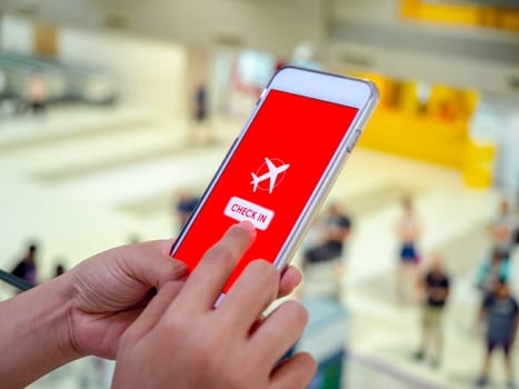 Flight check-in by mobile phone. Hand touching on smartphone screen to check-in for a flight in terminal airport.