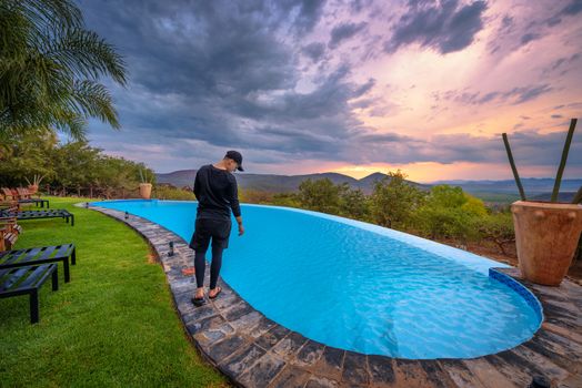 Opuwo, Namibia - March 31, 2019 : Girl dressed in black standing beside a swimming pool in the luxury Opuwo Country Lodge at sunset. Opuwo is the capital of the Kunene Region in north-western Namibia.