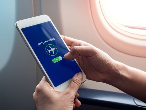Flight mode concept. Finger sliding on screen for turned on airplane mode near the window on the airplane.