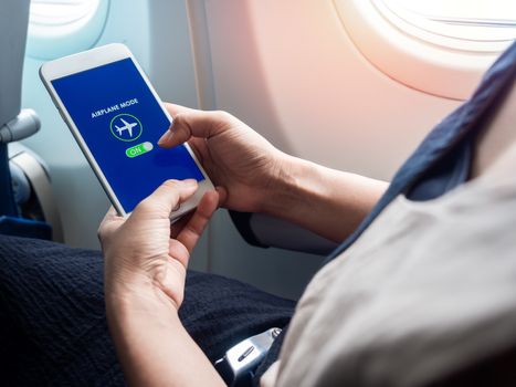 Flight mode concept. Hand holding white smartphone and turned on airplane mode on screen near the window on the airplane.