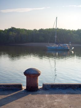 Old bollard without mooring rope on concrete port on riverside with yacht on the sea on mangrove forest background vertical style.