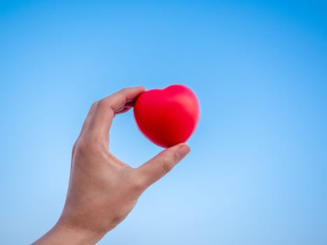 Red heart in hand on blue sky background, love, peace and giving concept.