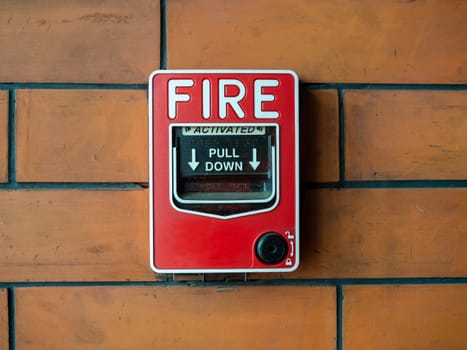 Red manual pull fire alarm safety system. Close-up pull station or call point, manual fire alarm activation on brick wall background.