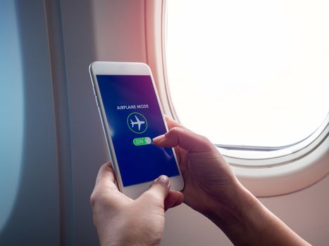 Flight mode concept. Finger sliding on screen for turned on airplane mode near the window on the airplane with copy space.