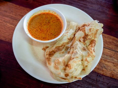 Breakfast Thai southern style. Delicious roti with coconut milk curry in white dish on wooden table, top view.