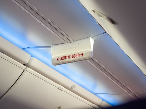 Emergency exit sign in airplane. Word red color in Thai language mean exit way on sign hanging on ceiling for passenger in cabin economy class on the low cost commercial airplane.