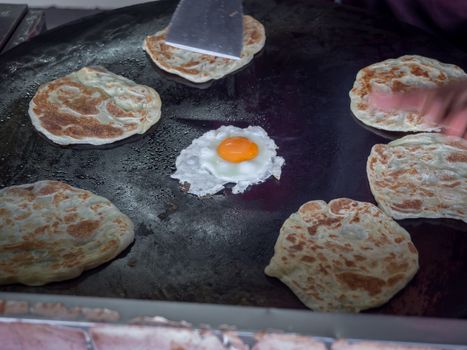 Roti Making, roti thresh flour by roti maker with oil. Indian traditional street food. Roti and egg fried on the pan.