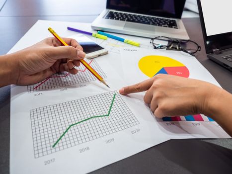 Business goal concept. Hands pointing diagrams graphs with pencil and business accessory, smartphone, laptop computer, glasses and highlighter pen on table.