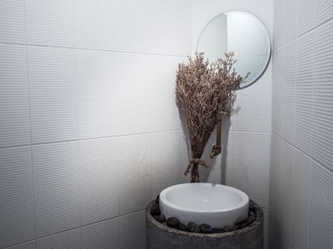 Bathroom decoration with narrow spaces. Vintage dried flowers near round mirror, bath sink and traditional faucet in the bathroom corner with copy space.