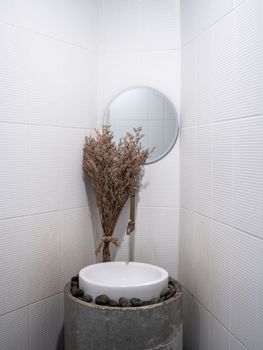 Bathroom decoration with narrow spaces. Vintage dried flowers near round mirror, bath sink and traditional faucet in the bathroom corner.