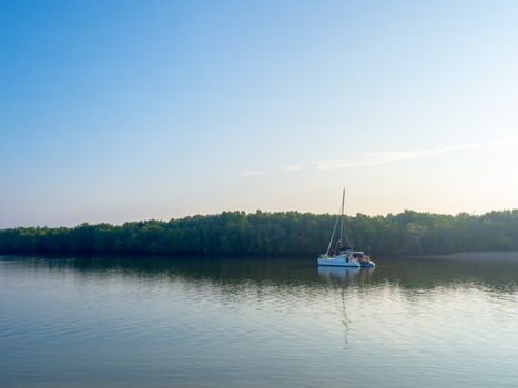 Lonely yacht on blue peaceful lake on green forest and blue sky background in the morning.