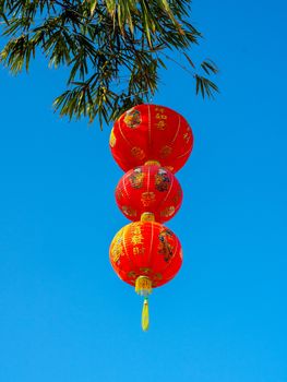 Red Chinese hanging lanterns on bamboo tree on blue sky background,  decoration for Chinese New Year vertical style. The text on lantern is meant as a greeting.