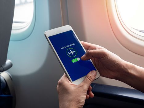 Flight mode concept. Finger sliding on screen for turned on airplane mode near the window on the airplane.