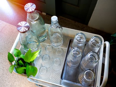 Free drinking water self service set in cafe. Pile of glass in tray and bottles of drinking water on trolley decoration with green plant, top view.