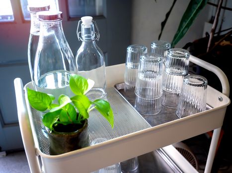 Free drinking water self service set in cafe. Pile of glass in tray and bottles of drinking water on trolley decoration with green plant.