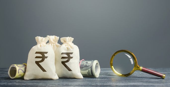 Indian rupee money bags and magnifying glass. Profitable investment, dividends payouts. Financial monitoring of suspicious cash transactions. Search sources of financing projects. Budget revision