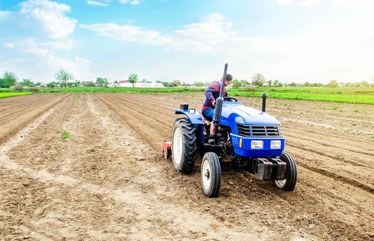 A farmer riding a tractor on a farm field. Farming and work in the agricultural industry. Cultivating land soil for further planting. Using technology to facilitate work and increase efficiency