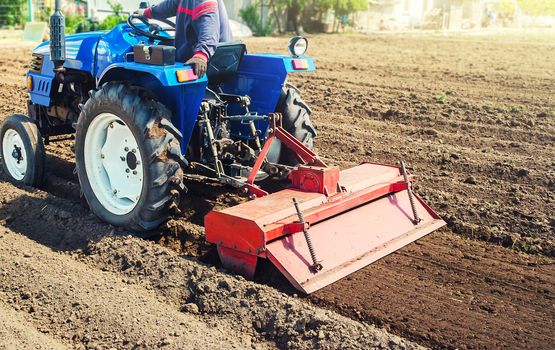 Farmer on a tractor cultivates land after harvesting. Grinding loosening plowing crumbling soil for further sowing by cultivated plants. Mechanization, development of agricultural technologies.