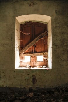 Window of an abandoned house taken from inside; the light illuminates the room a little, leaving a glimpse of the cobwebs and the peeling wall