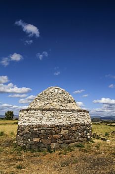 An ancient stone construction, a Sardinian nuraghe, stands out against the clear blue sky of Sardinia