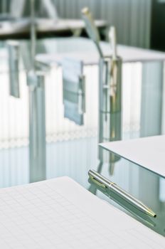 Waiting for the meeting. The crystal table set with paper pads for notes, pens and business cards reflects the curtains with vertical strips that cut the light of the large windows