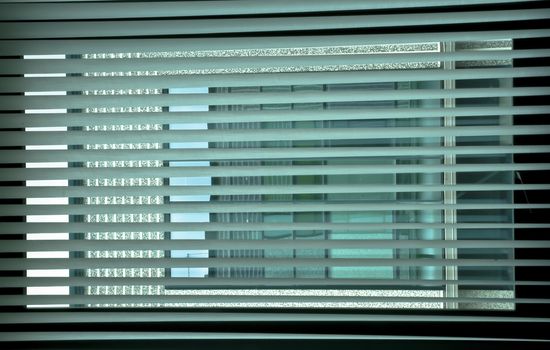 Geometries at the window. Venetian blinds at the office window create an interesting game of colors and colors by drawing a grid on the colored windows of the building opposite