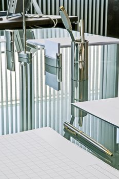 Waiting for the meeting. The crystal table set with paper pads for notes, pens and business cards reflects the curtains with vertical strips that cut the light of the large windows