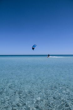 San Teodoro - La Cinta Beach - 2017 July - A kitesurf with its sail and the board, cuts the line that divides the blue sky from the crystalline sea of Sardinia