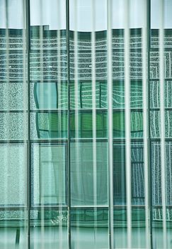 Geometries at the window. Window vertical blinds at the office window create an interesting game of colors and colors by drawing a grid on the colored windows of the building opposite