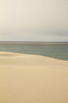 The gray sky breaks abruptly on the winter sea harmoniously marked by the yellow sand dune