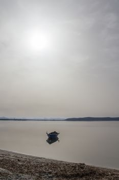 Fishing boat anchored in a sea bay with flat water that merges with the white sky