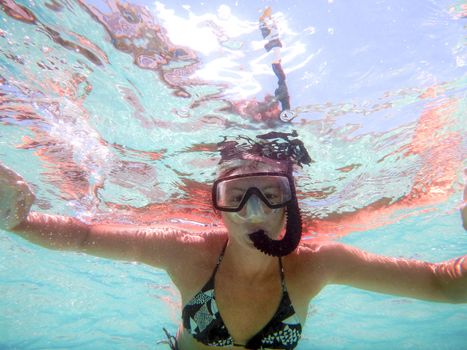 Young woman shooting in water from below with open arms with mask and snorkel in a beautiful game of colored water reflections