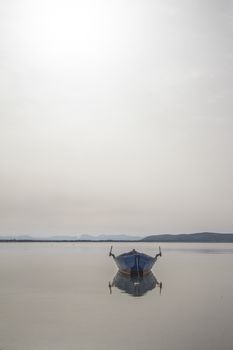 Fishing boat anchored in a sea bay with flat water that merges with the white sky