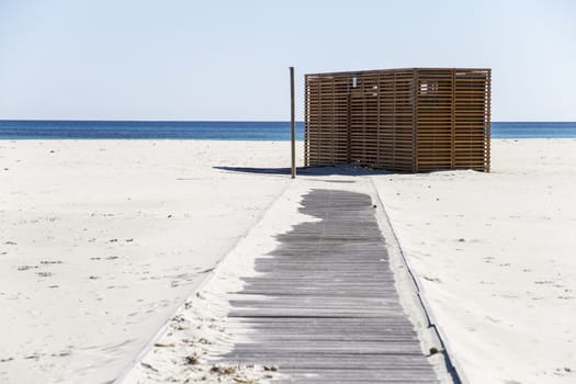 Baracca wooden bar, closed, on the deserted white beach with the blue sea from Sardinia in the background