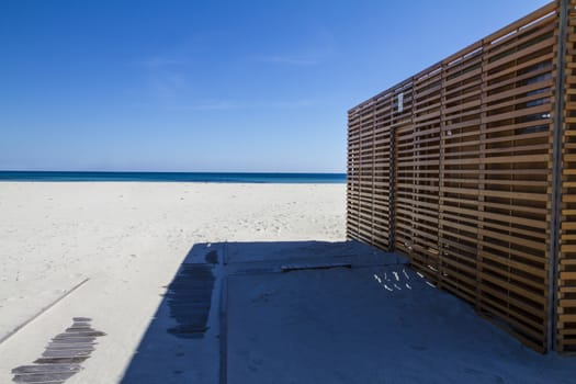 Baracca wooden bar, closed, on the deserted white beach with the blue sea from Sardinia in the background