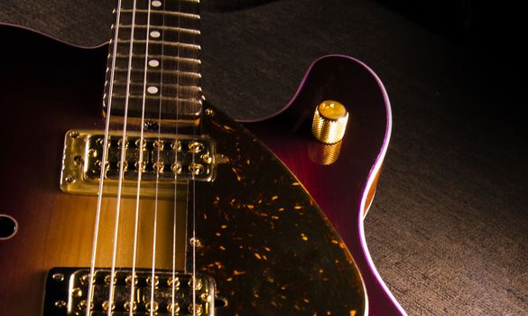 Closeup of sunburst electric guitar with brass mechanics and bright colors on a dark shaded background