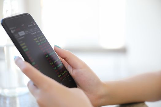 Close up on woman hand holding smartphone trading stock and data in coffee shop background business concept