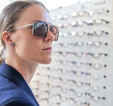 A young attractive woman in an optics store tries on new glasses.