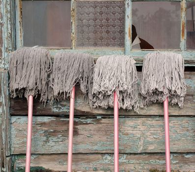 Four Chinese style mops are leaning against an old house so they can dry
