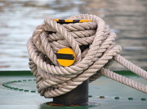 A thick rope is wrapped around a strong post on deck of a ship
