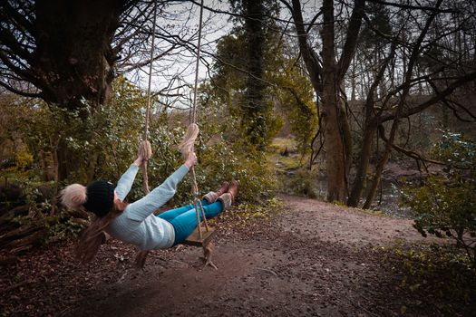 Young woman swinging on a home made swing out in the woods