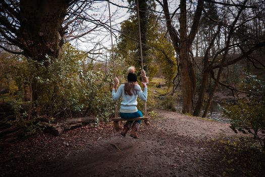 Young woman swinging on a home made swing out in the woods