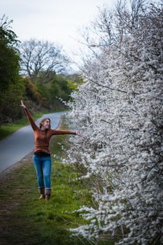 A young attractive woman posing beside a white cherry blossom tree on a country footpath