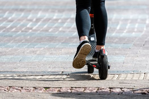 Legs of a woman on a electric kick scooter, rear view