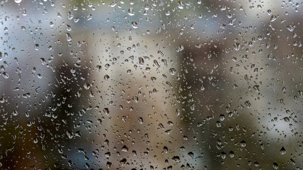 View of the city in a rainy day through a window covered with water drops - image